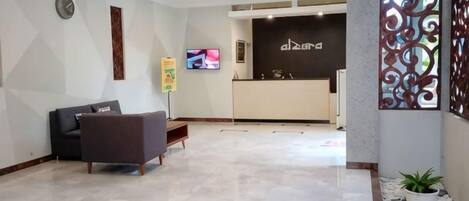 A hotel reception area with a reception desk, a television, and a seating area with a sofa and a bench.