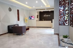 A hotel reception area with a reception desk, a television, and a seating area with a sofa and a bench. - Alzara Hotel Syariah (Wonosari)