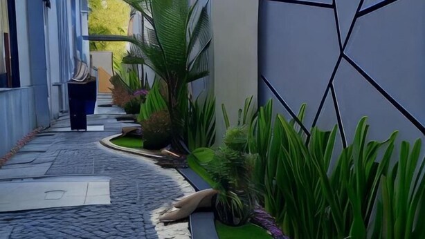 A narrow, paved pathway flanked by lush green plants and a modern building with geometric wall design. - Alzara Hotel Syariah (Wonosari)