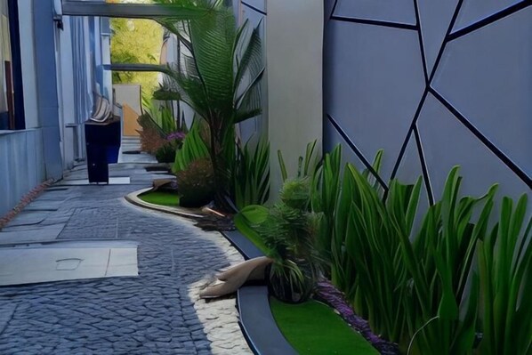 Un estrecho sendero pavimentado bordeado por exuberante vegetación y un edificio moderno con diseño geométrico en la pared.