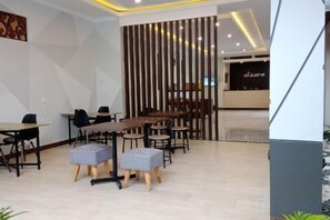 A modern conference room with tables and chairs, a decorative wall, and a reception area in the background. - Alzara Hotel Syariah (Wonosari)