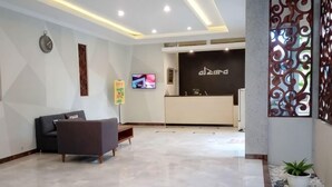 A hotel lobby with a reception desk, a TV screen, a sofa, and a decorative wall. - Alzara Hotel Syariah (Wonosari)