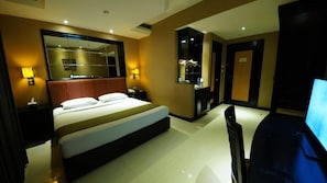 A hotel room with a large bed, bedside lamps, a TV, and a mirror. - Tematik Hotel Pluit (Jakarta)