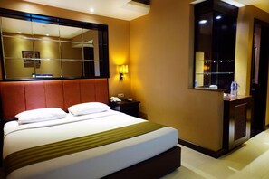 A hotel room with a large bed, a bedside table, a mirror, and a wall-mounted air conditioning unit. - Tematik Hotel Pluit (Jakarta)