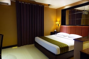 A hotel room with a bed, a nightstand, a lamp, a window with curtains, and a mirror. - Tematik Hotel Pluit (Jakarta)