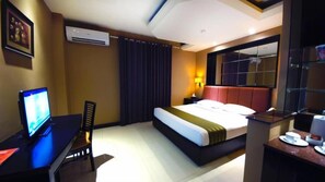 A hotel room with a bed, a desk with a computer, a television, and a window with curtains. - Tematik Hotel Pluit (Jakarta)