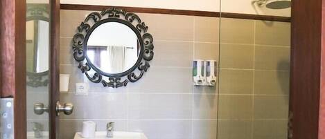 A bathroom with a glass shower enclosure, a white sink, and a decorative mirror.