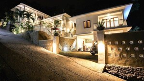 A modern two-story house with a well-lit entrance, a staircase, and a balcony. - Dewivilla Hotel (Padangbai)