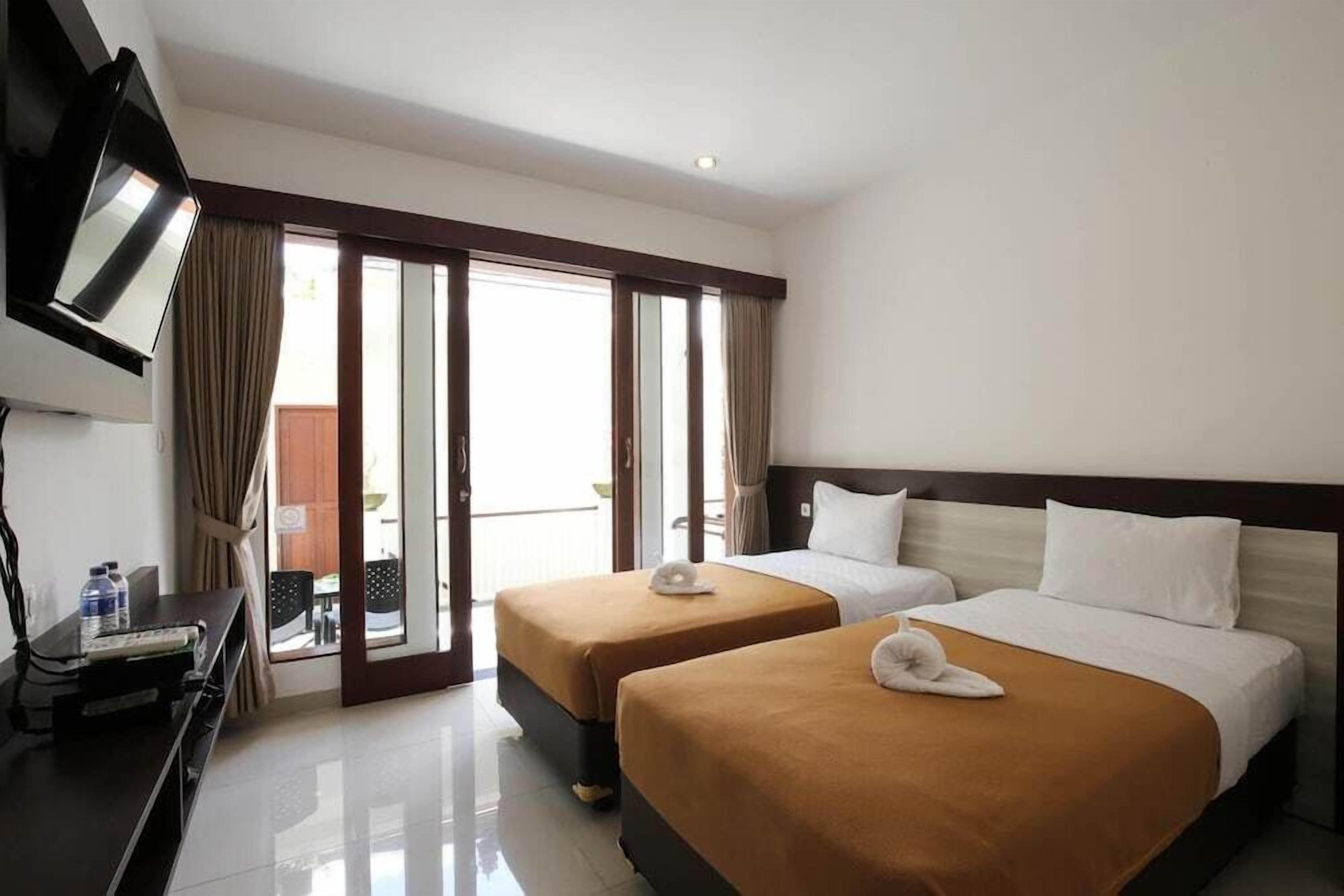 A hotel room with two beds, a TV, a desk with a computer, and a sliding glass door to the outside.