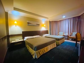 A hotel room with two beds, a desk, a chair, and a large window with curtains. - Hotel Grand Crystal Kedah (Alor Setar)