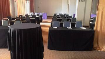 A conference room with round tables and chairs, a stage, and a curtain.