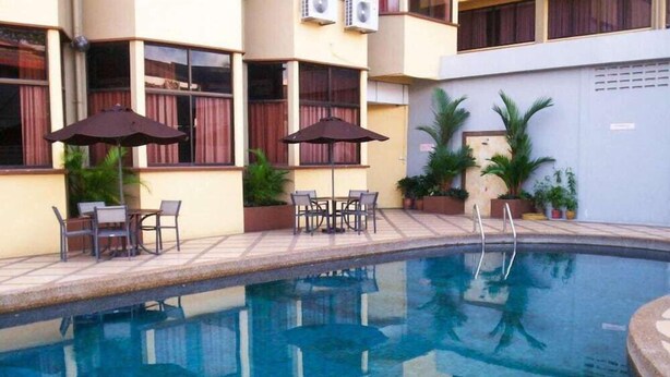 A swimming pool with lounge chairs and umbrellas, surrounded by potted plants and a building with windows and air conditioning units. - Hotel Grand Crystal Kedah (Alor Setar)