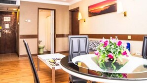 A hotel room with a round table, chairs, a flower arrangement, a painting on the wall, and a door leading to another room. - Hotel Grand Crystal Kedah (Alor Setar)