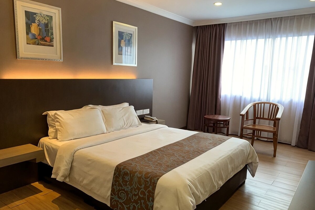 A hotel room with a large bed, a bedside table, a chair, and a window with curtains.