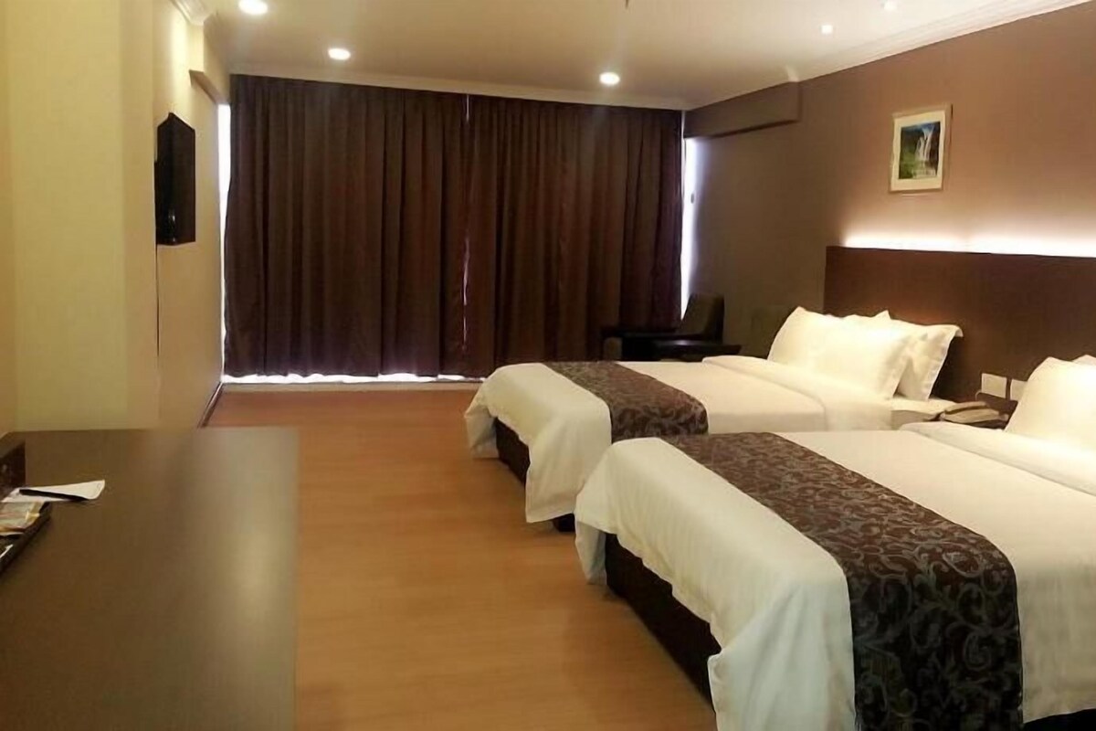 A hotel room with two beds, a desk, and a large window with curtains.
