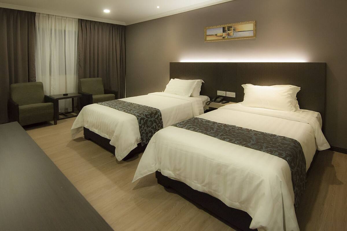 A hotel room with two beds, a desk, a chair, a nightstand with a phone, and a painting on the wall.