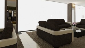 A modern living room with a sectional sofa, a coffee table, and a large mirror. - Hotel Anika (Kluang)