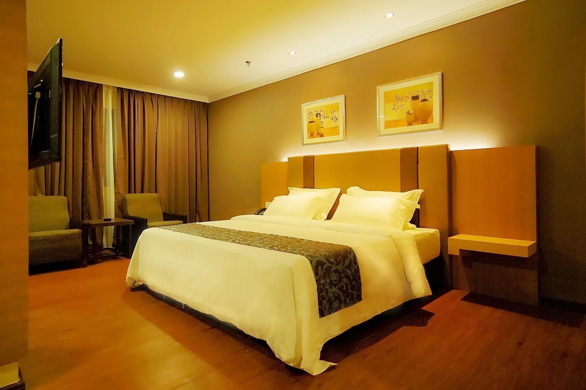 A hotel room with a large bed, a television, a desk, and two wall-mounted lamps.