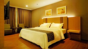 Una habitación de hotel con una cama grande, un televisor, un escritorio y dos lámparas fijadas a la pared.