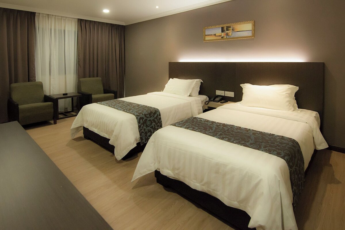 A hotel room with two beds, a desk, a chair, and a painting on the wall.