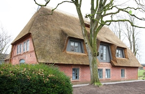 Une maison traditionnelle à toit de chaume, avec une façade en briques, de nombreuses fenêtres et un jardin bien entretenu.