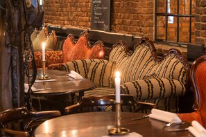 Un restaurant à l’ambiance chaleureuse, avec un mur en briques, des sièges confortables et une bougie sur la table.