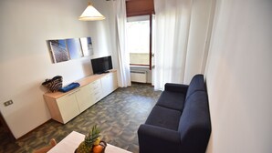 Ein modernes Wohnzimmer mit einer Couch, einem Esstisch mit Obst, einem Fernseher und einem weißen Schrank.