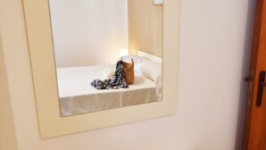 Ein Badezimmer mit Spiegel, Waschbecken und Pflegeprodukten, wobei ein Bett im Spiegelbild zu sehen ist.