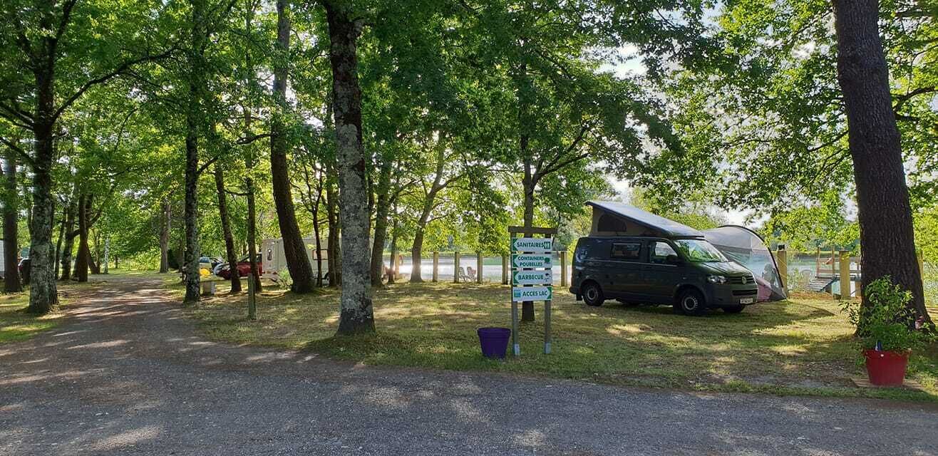 Un terrain de camping équipé d’un emplacement pour camping-car et d’un panneau indiquant les commodités disponibles, comme un barbecue et un espace pique-nique.