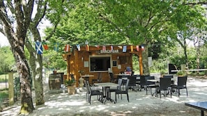 A snack bar with outdoor seating, surrounded by trees and potted plants. - Camping Le Chene Du Lac (Bayas)