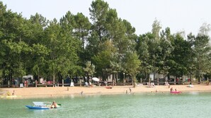A beach with a row of cabins and a boat on the water. - Camping Le Chene Du Lac (Bayas)