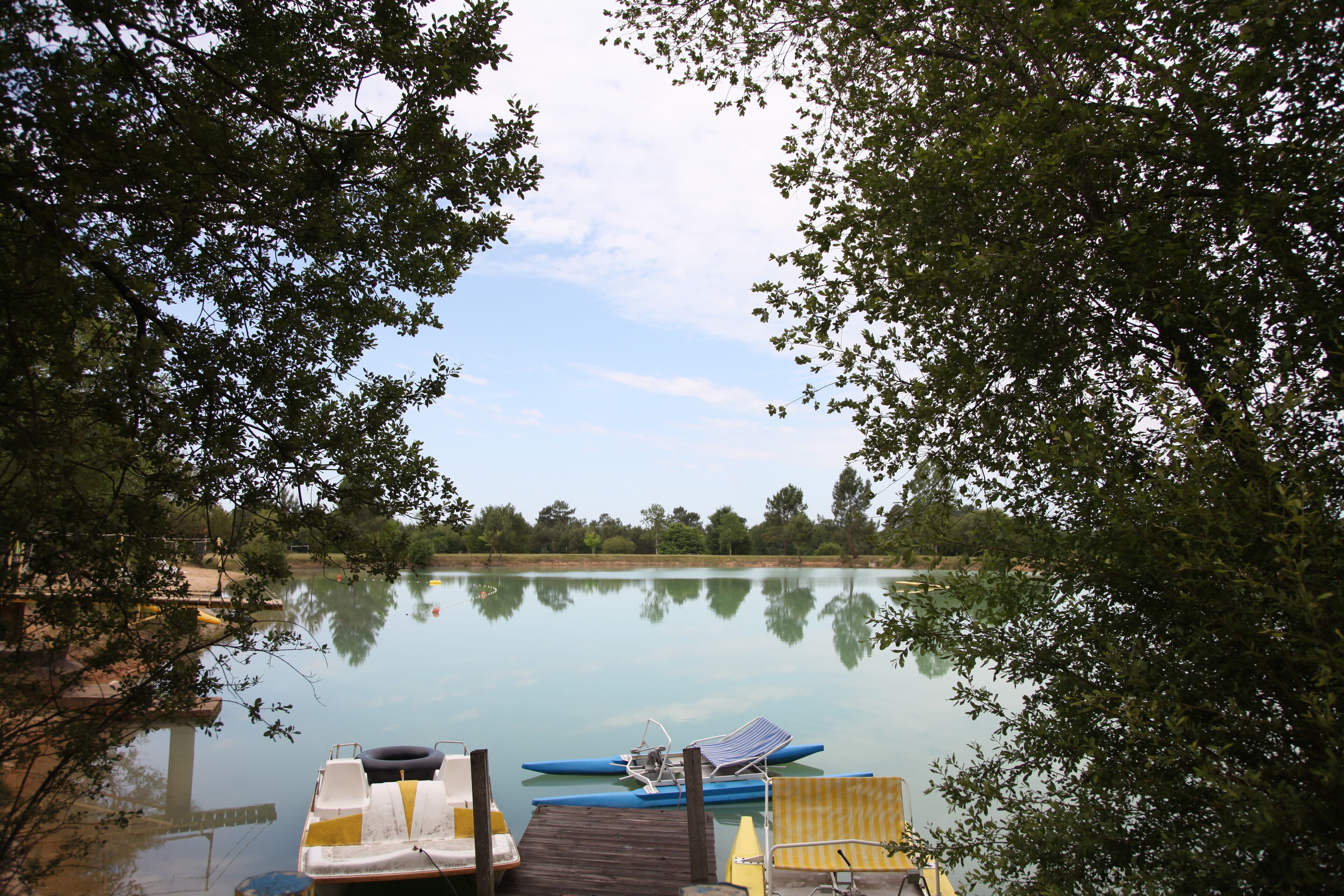 Un llac tranquil amb un moll, un cànoi blau i una cadira groga.