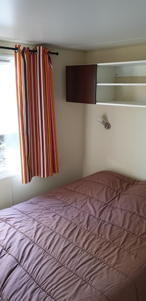 A bedroom with a bed, a striped curtain, a cabinet, and a window. - Camping Le Chene Du Lac (Bayas)