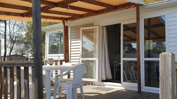 A covered deck with a table and chairs, wooden railings, and sliding glass doors leading to an interior space. - Camping Le Chene Du Lac (Bayas)