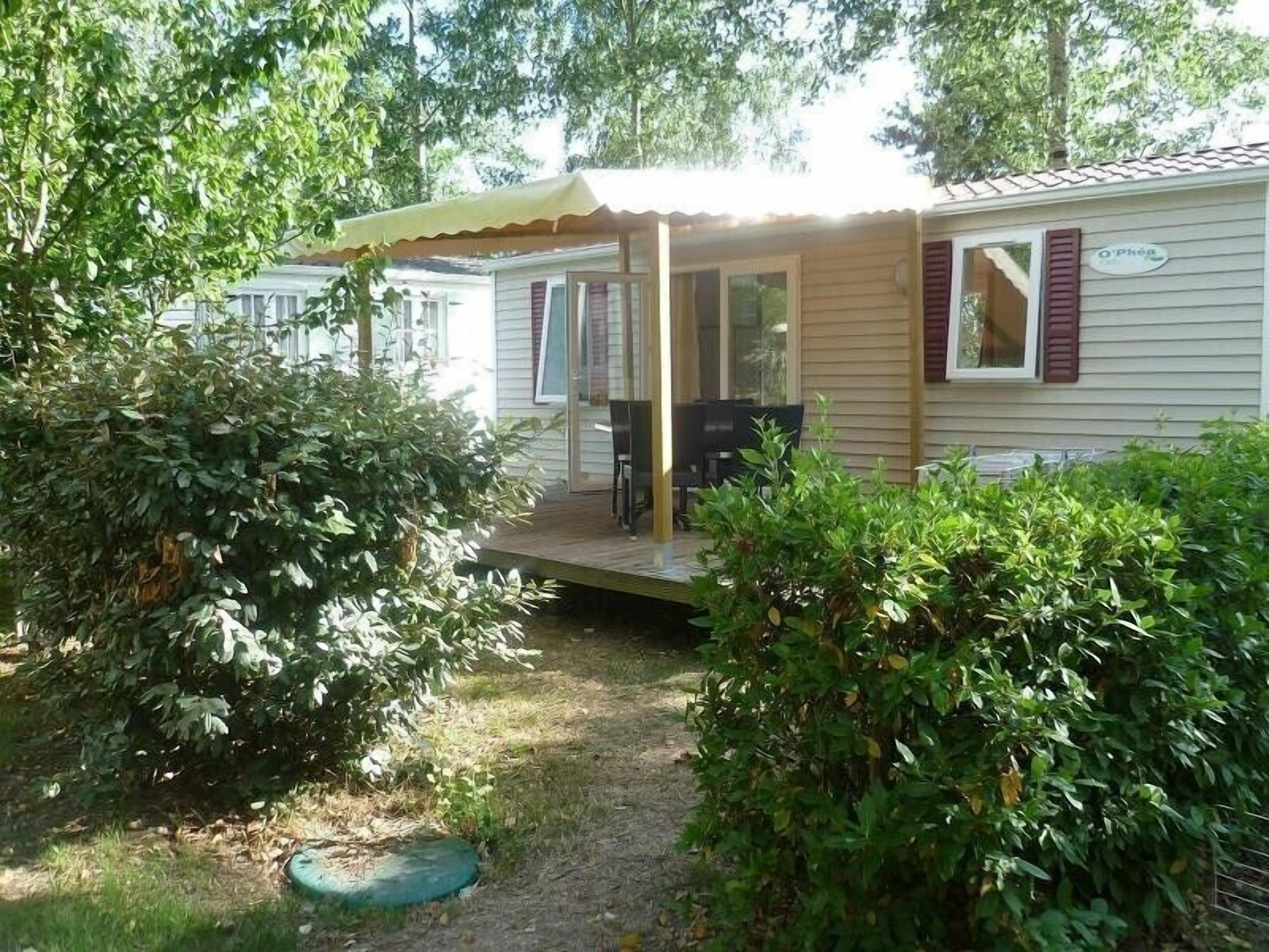 A mobile home with a covered patio, a small table and chairs, and a window with shutters.