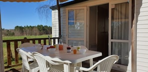 A white table with chairs on a deck, a bottle of juice, and bowls of food. - Camping Le Chene Du Lac (Bayas)