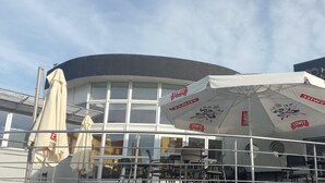 Un bâtiment à la façade incurvée, doté de grandes fenêtres et d’un espace extérieur aménagé avec des parasols.