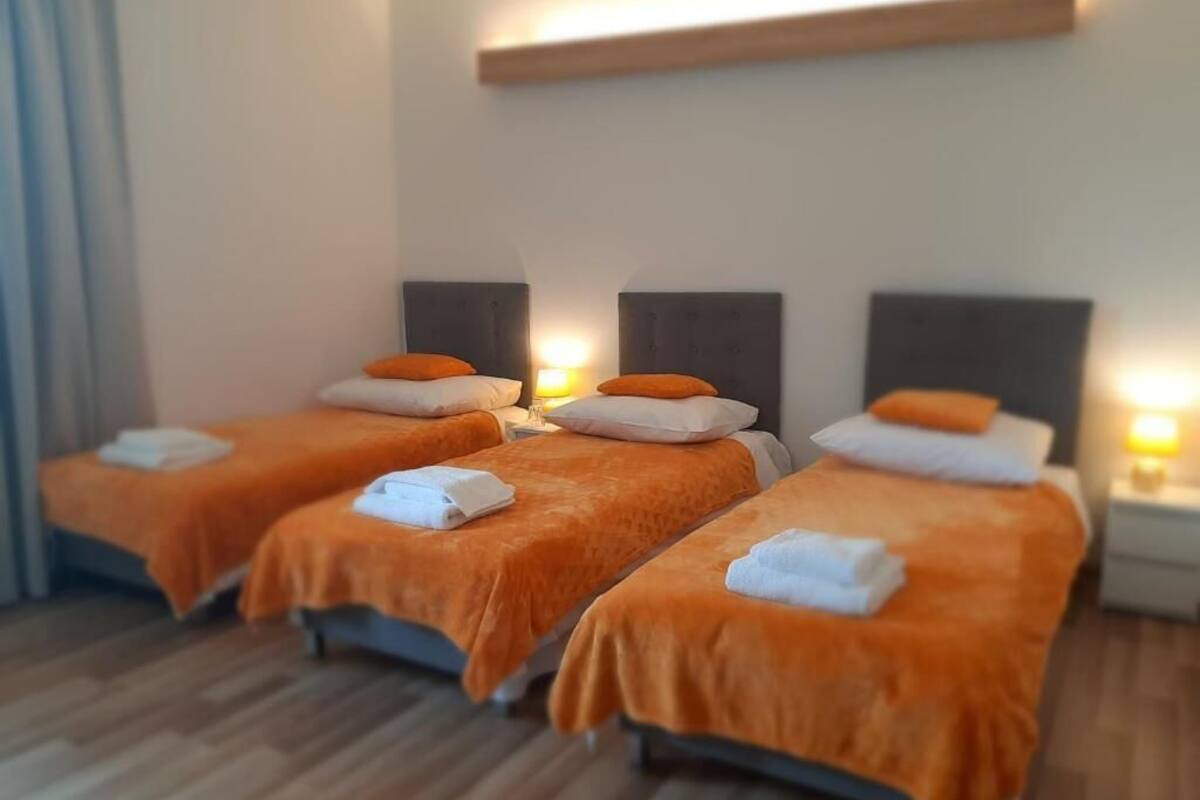 Une chambre d’hôtel avec trois lits, chacun recouvert d’une couverture orange et doté d’oreillers blancs.