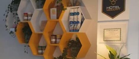 Um balcão de recepção com uma estante hexagonal amarela exibindo diversos objetos, uma luminária e uma pequena estatueta de coelho.
