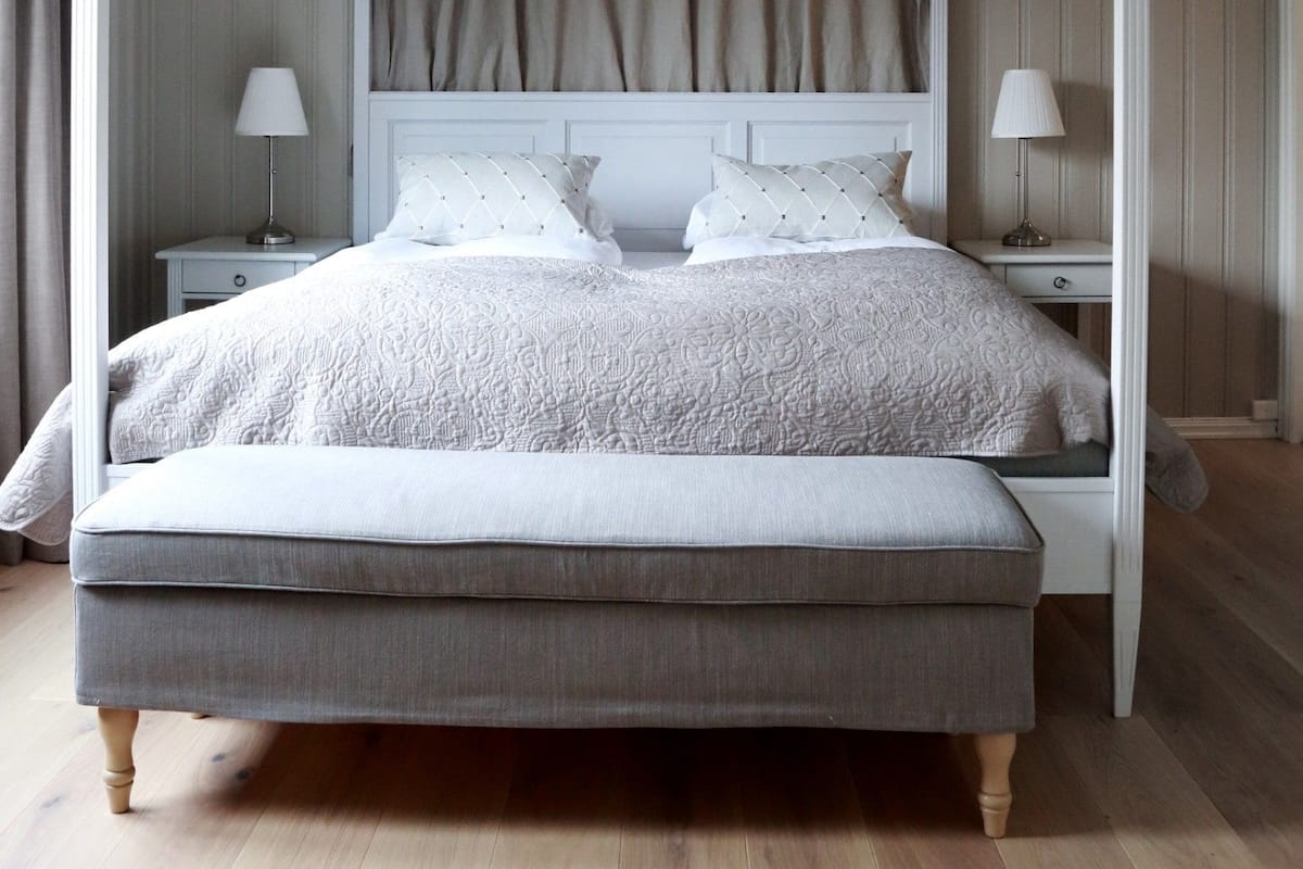 A four-poster canopy bed with a tufted headboard, two bedside tables with lamps, and a bench at the foot of the bed.