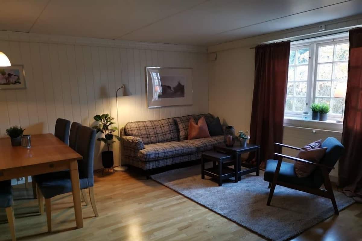 A cozy living room with a wooden dining table, a plaid sofa, a blue armchair, and a small coffee table.