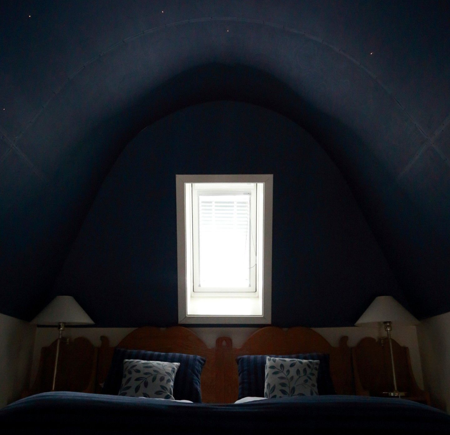 A bedroom with a sloped ceiling, a window, a bed with pillows, and bedside lamps.
