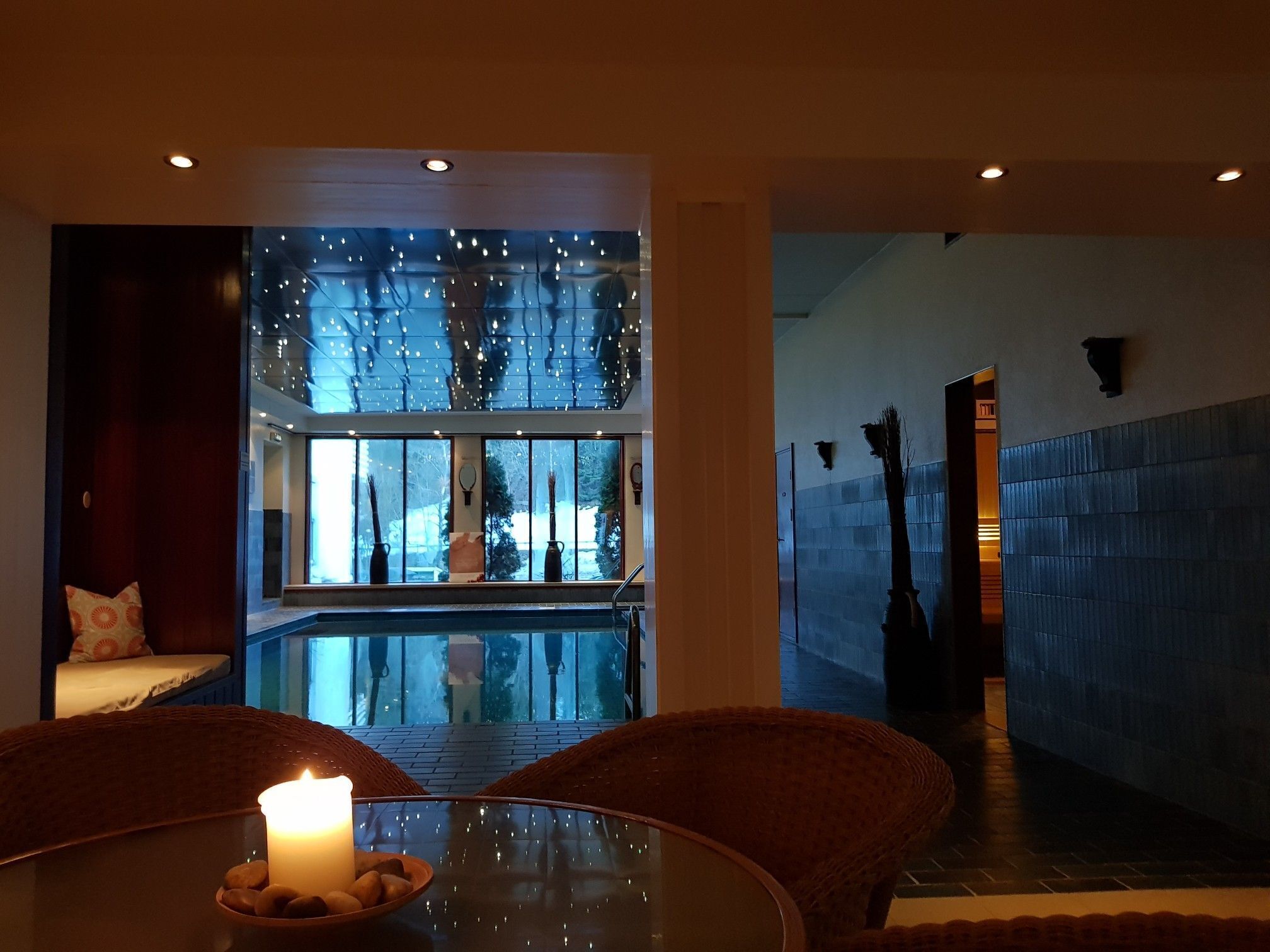 A modern interior with a glass table, a lit candle, and a view of a pool area.