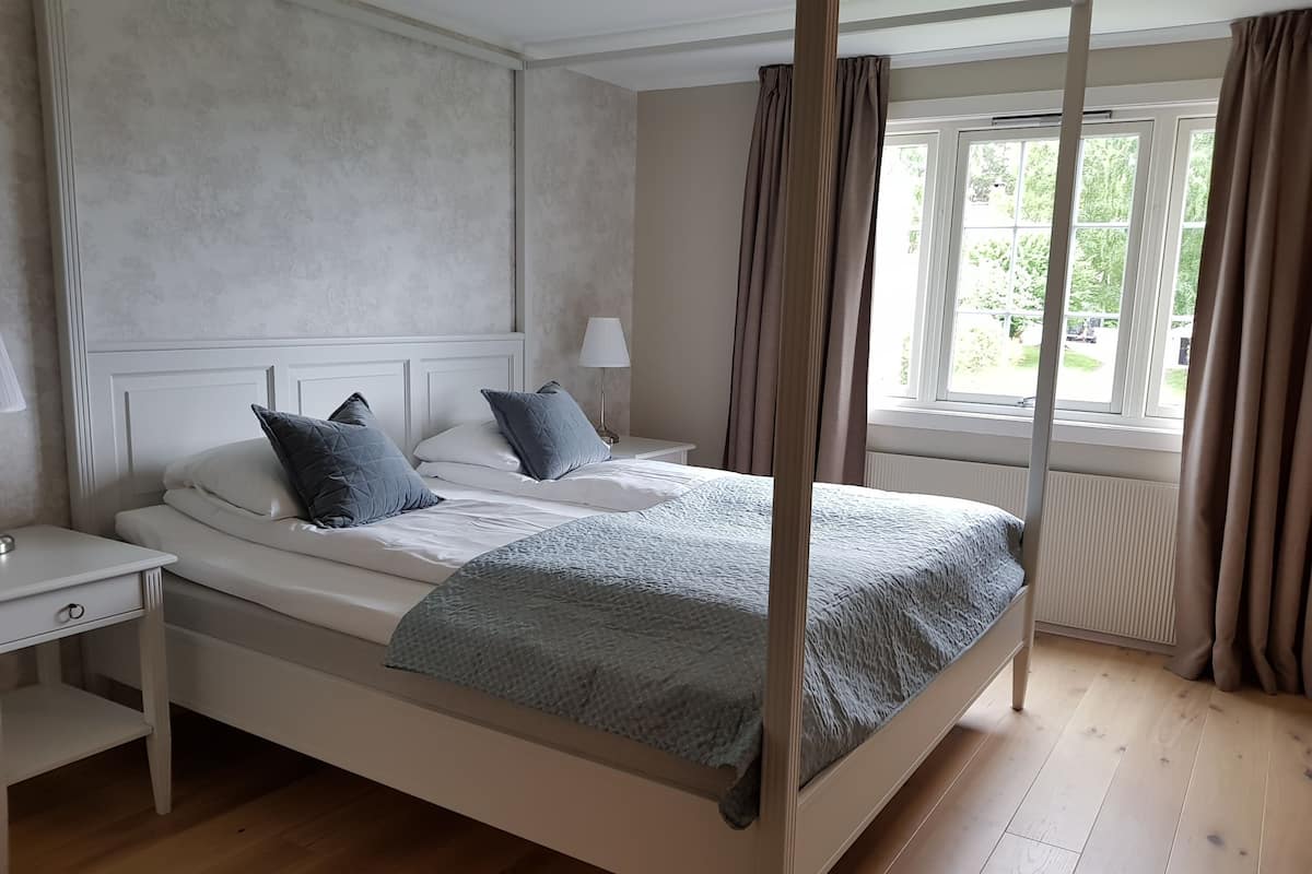 A four-poster bed with a grey quilt, two pillows, and a bedside table with a lamp.
