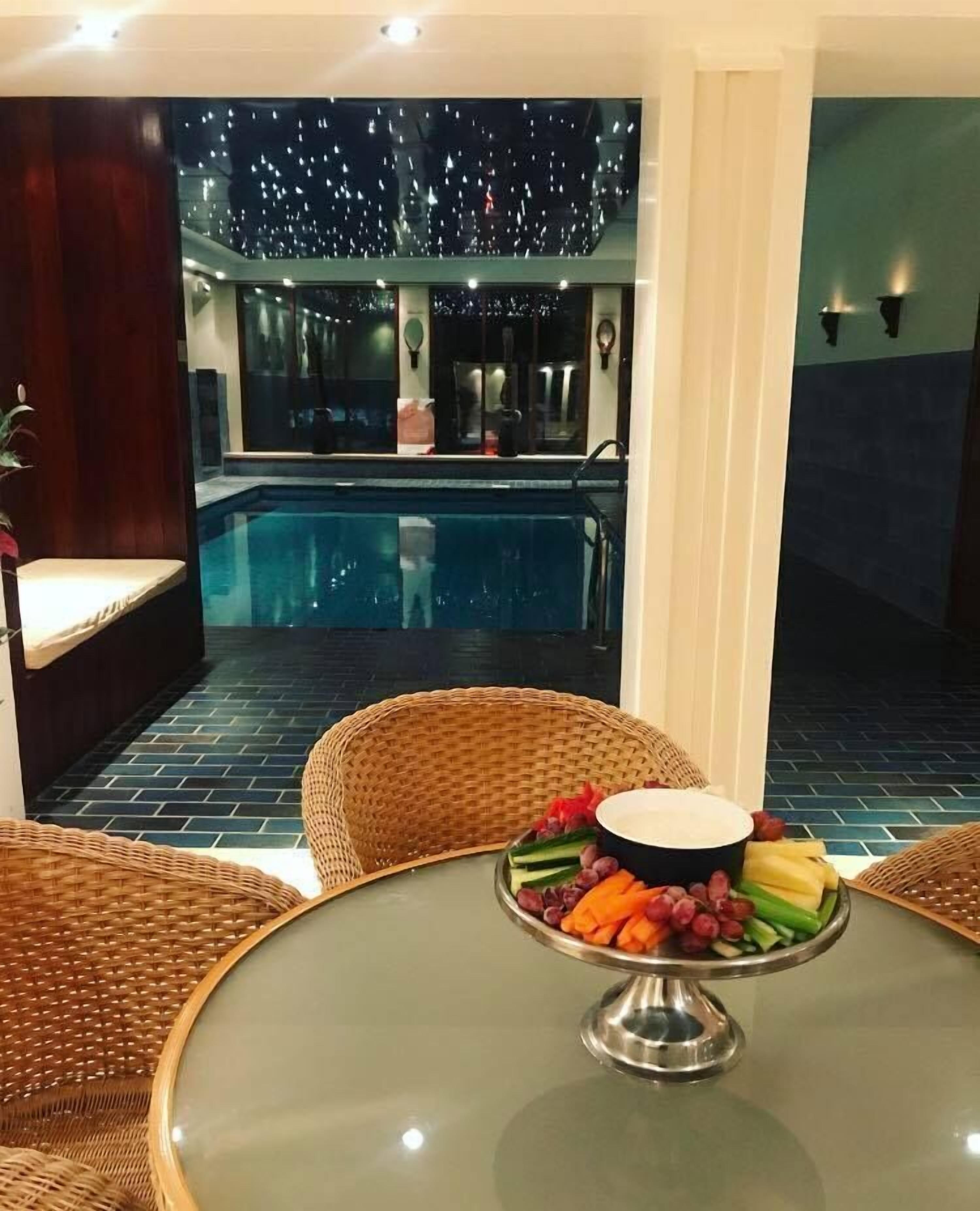 Un área de comedor junto a la piscina, con sillas de mimbre, una mesa de vidrio y una bandeja de frutas.