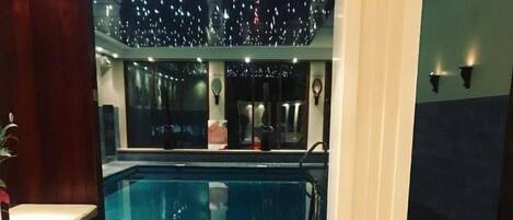 Un área de comedor junto a la piscina, con sillas de mimbre, una mesa de vidrio y una bandeja de frutas.