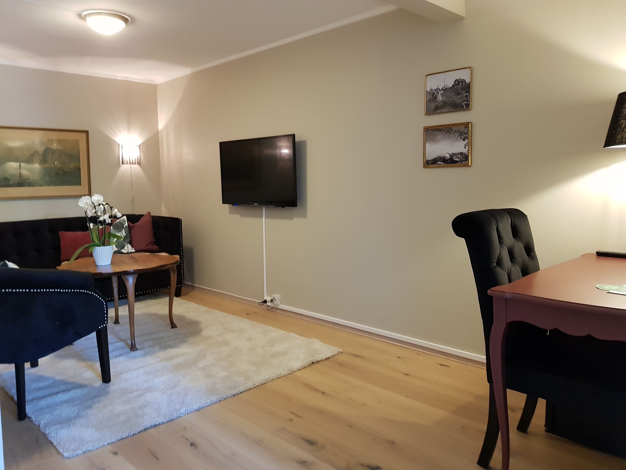 A living room with a sofa, a coffee table, a TV mounted on the wall, and a dining table with chairs.