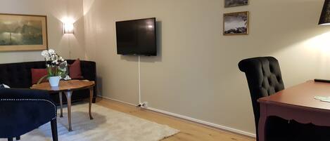 A living room with a sofa, a coffee table, a TV mounted on the wall, and a dining table with chairs.