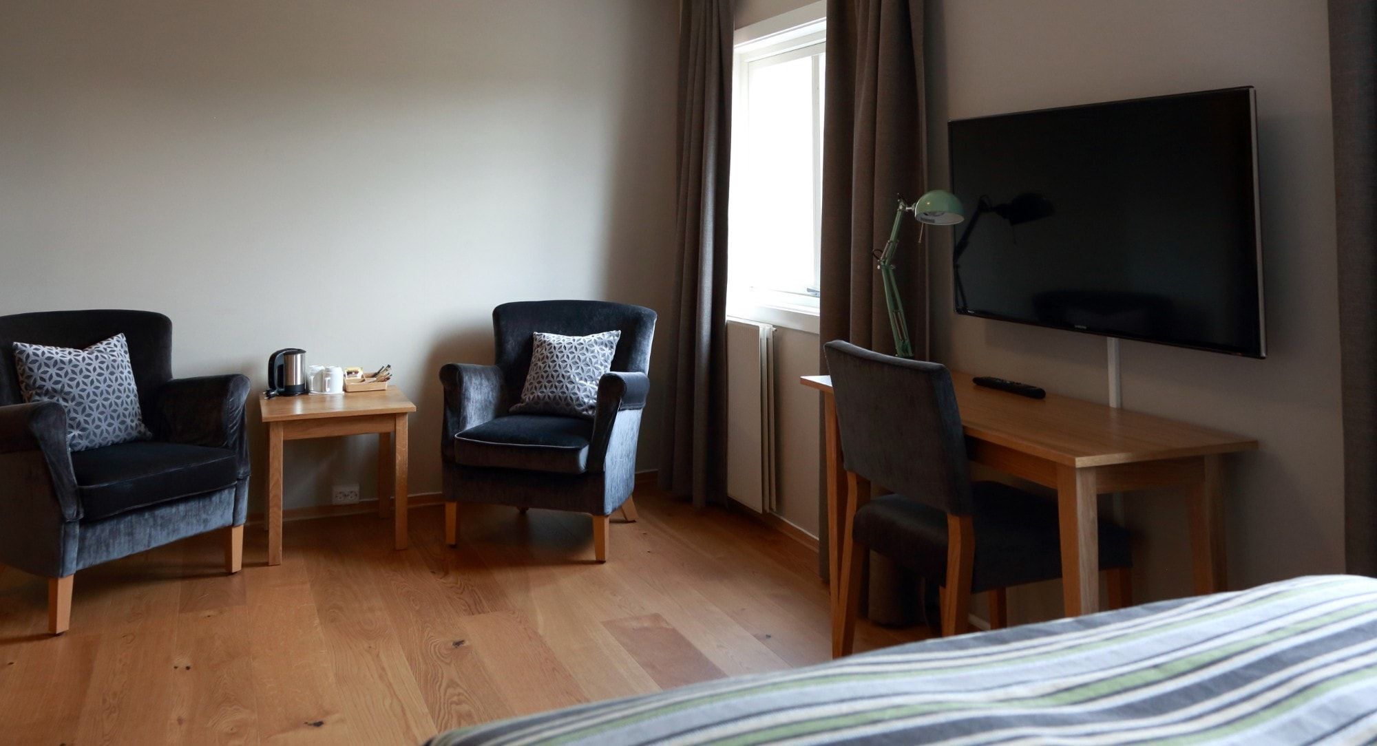 Habitación de hotel con cama, dos sillones, un escritorio, televisor y ventana con cortinas.