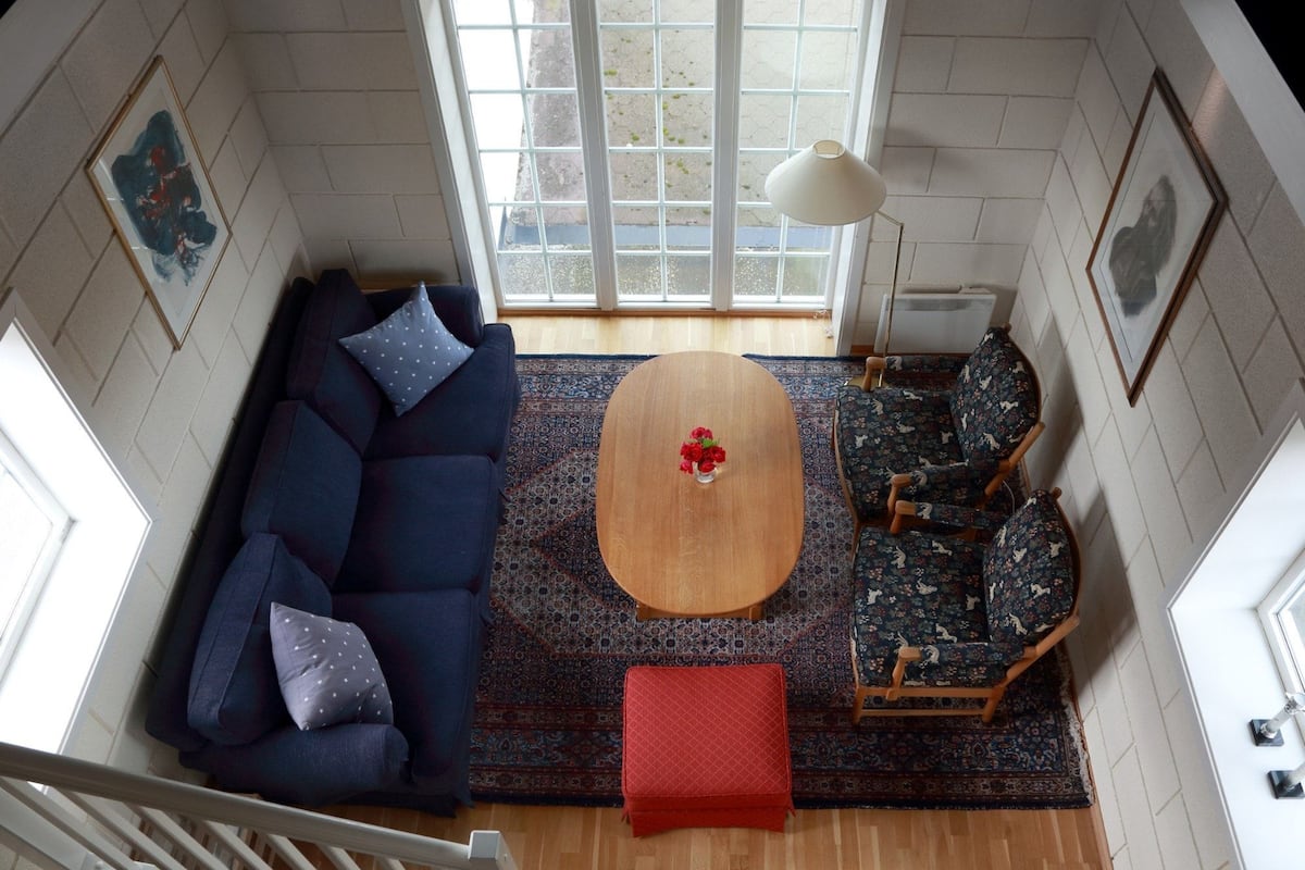 A living room with a blue sofa, patterned chairs, a wooden coffee table, and a red ottoman.